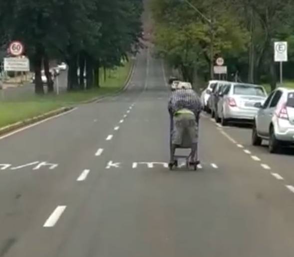 Homem desce avenida pilotando um carrinho de supermercado