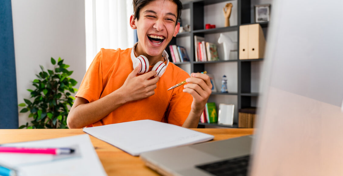 Teenage Boy With Headphones Having Online School Class At Home