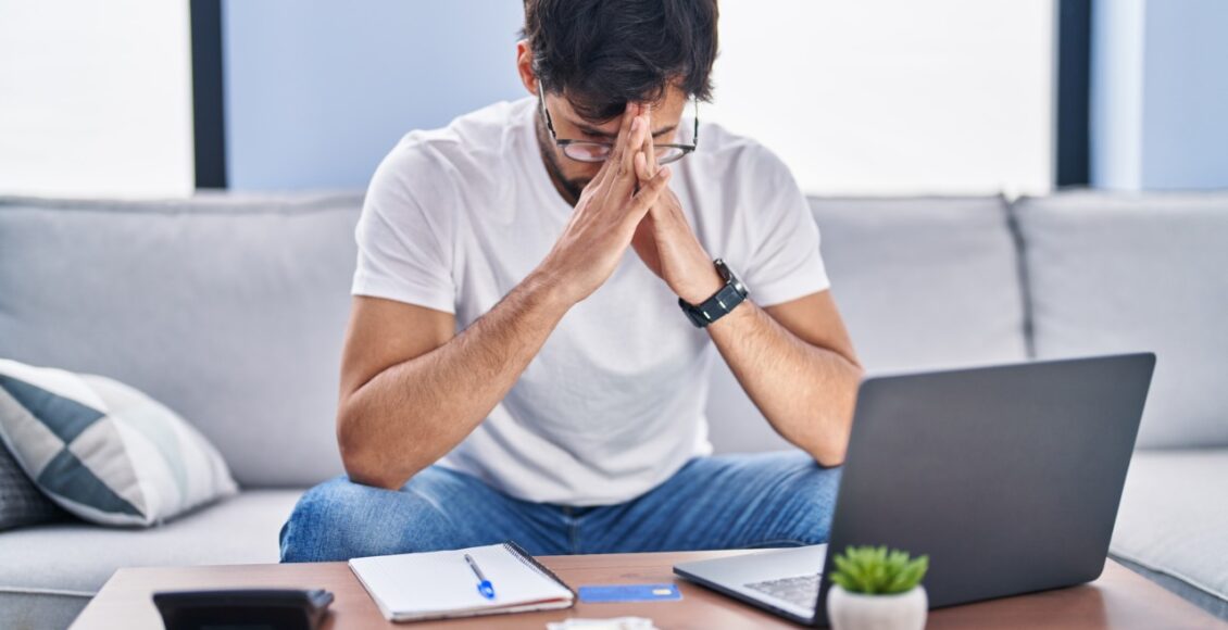 Young Hispanic Man Stressed Using Laptop Working At Home