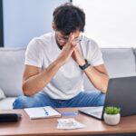 Young Hispanic Man Stressed Using Laptop Working At Home