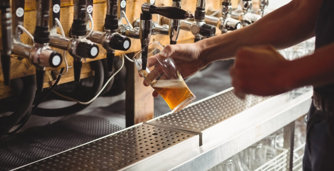 Mid Section Of Bar Tender Filling Beer From Bar Pump At Bar Counter