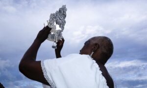 a foto mostra uma mulher negra segurando uma coroa para cima. Atrás, um céu azul